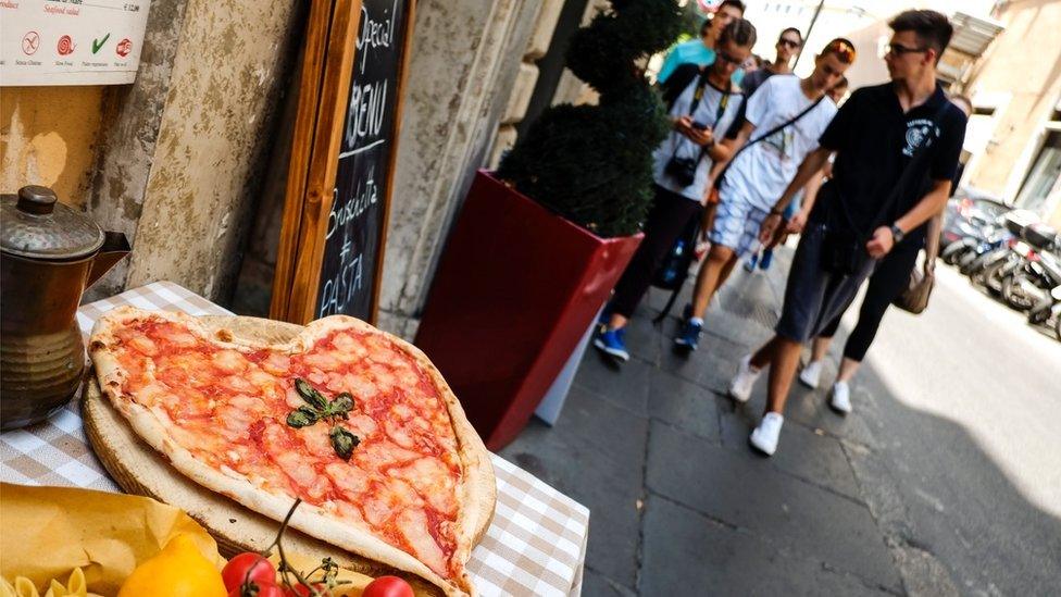 Tourists walk past a heart-shaped pizza, in central Rome on 2 August 2016