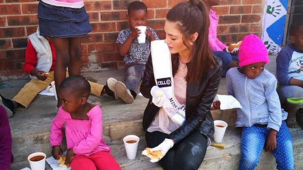 Miss South Africa wearing gloves with food around Soweto orphans