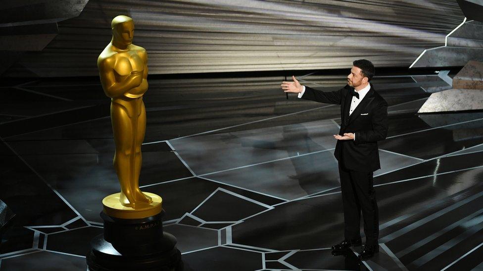 Jimmy Kimmel stands next to a giant Oscars statue