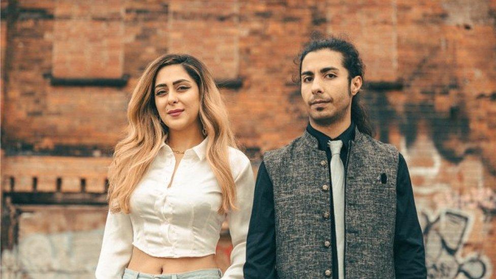 Iranian musicians Nasim Heidari and Omid Shir Mohammadi stand in front of a red brick wall