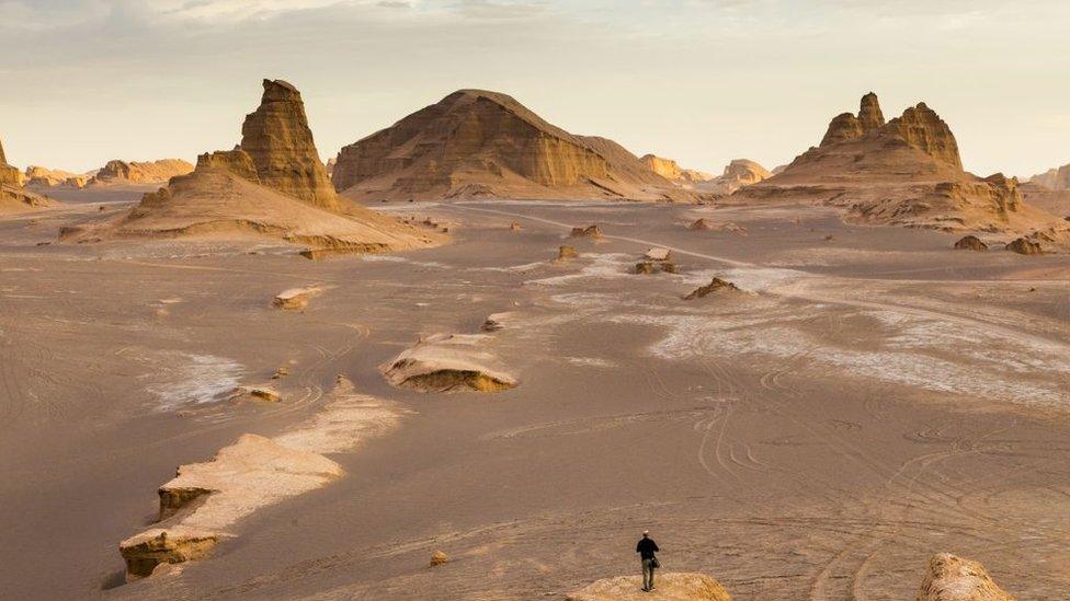 lut's empty landscape with mountains in the distance and a person looking out across the desert