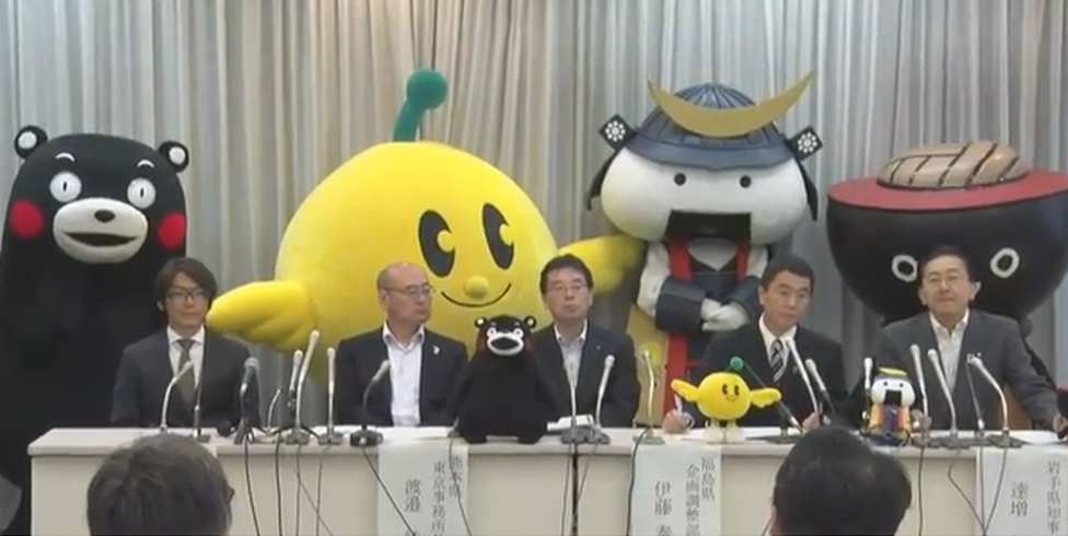 Officials at the press conference with the mascots standing behind them