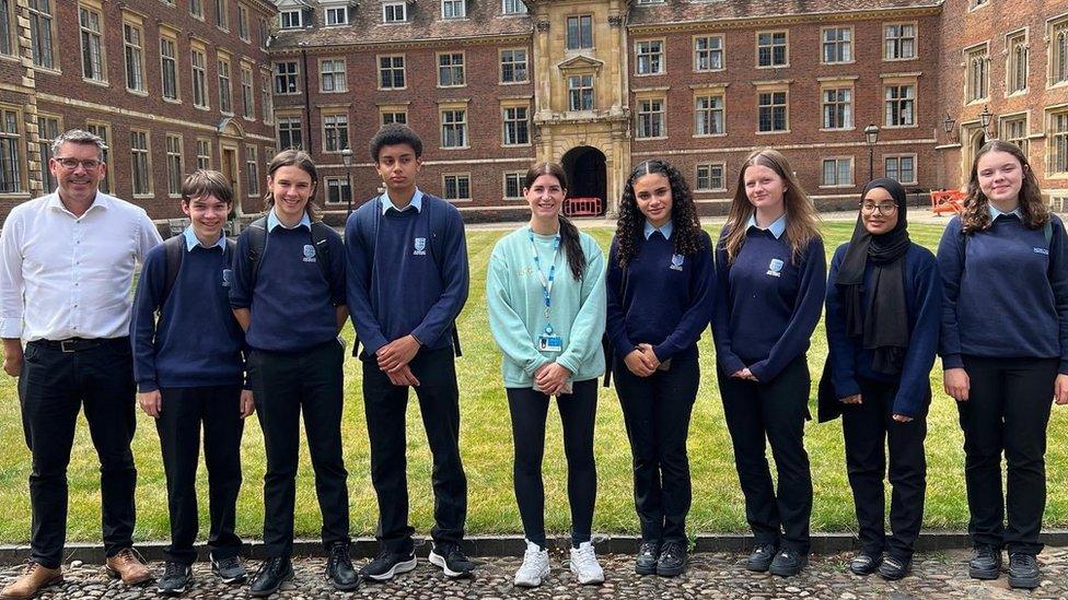 Seven pupils in blue school uniforms with two adults in a Cambridge court