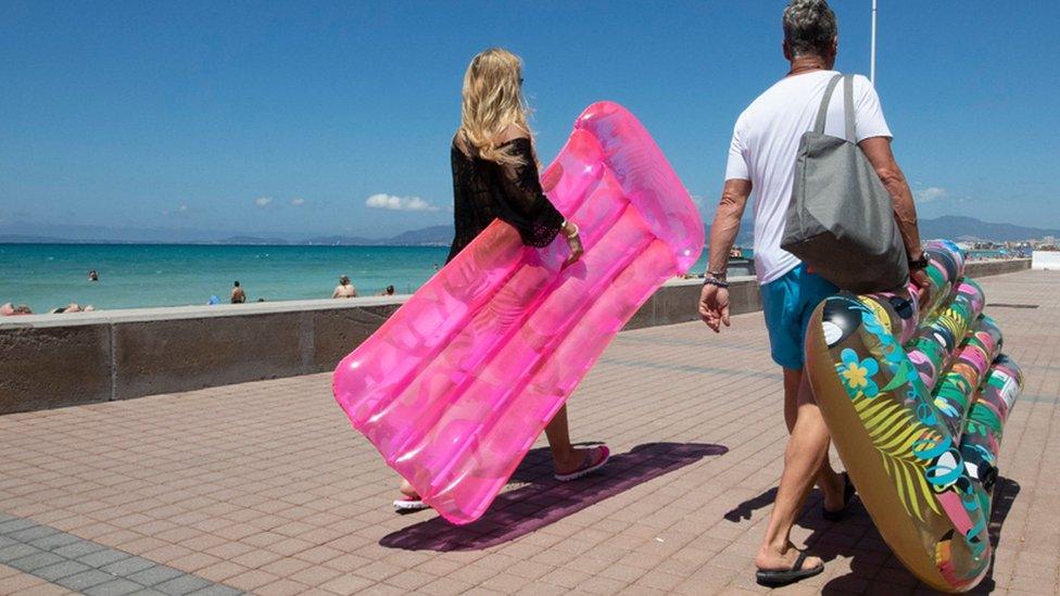 Tourists walk holding inflatable mattress at Palma Beach in Palma de Mallorca on June 7, 2021.