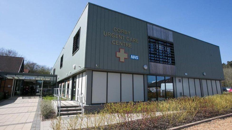The outside of Corby Urgent Care Centre. It is a grey box-like building which has an NHS logo on it. Writing on the side of the building reads, CORBY URGENT CARE CENTRE.