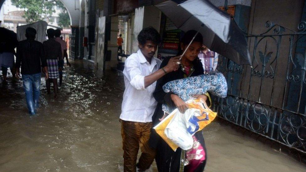 An Indian couple shelter under an umbrella as they walk with their child through floodwaters inundating Egmore Hospital in Chennai on December 1, 2015,