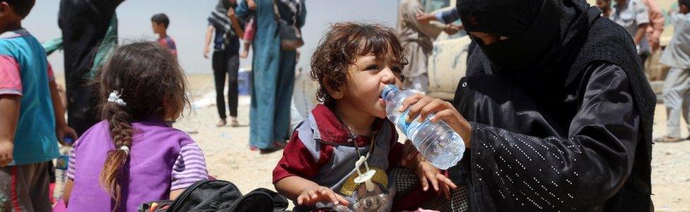 A displaced Iraqi woman helps a child drink water at a camp outside Irbil (15 July 2016)