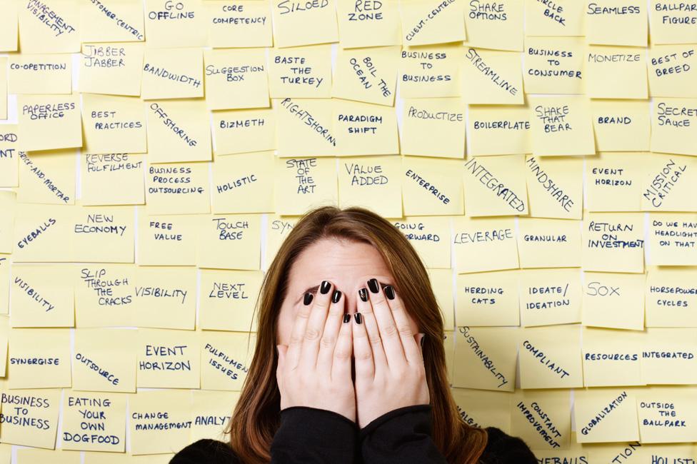 A woman covers her face in front of a wall covered with business jargon