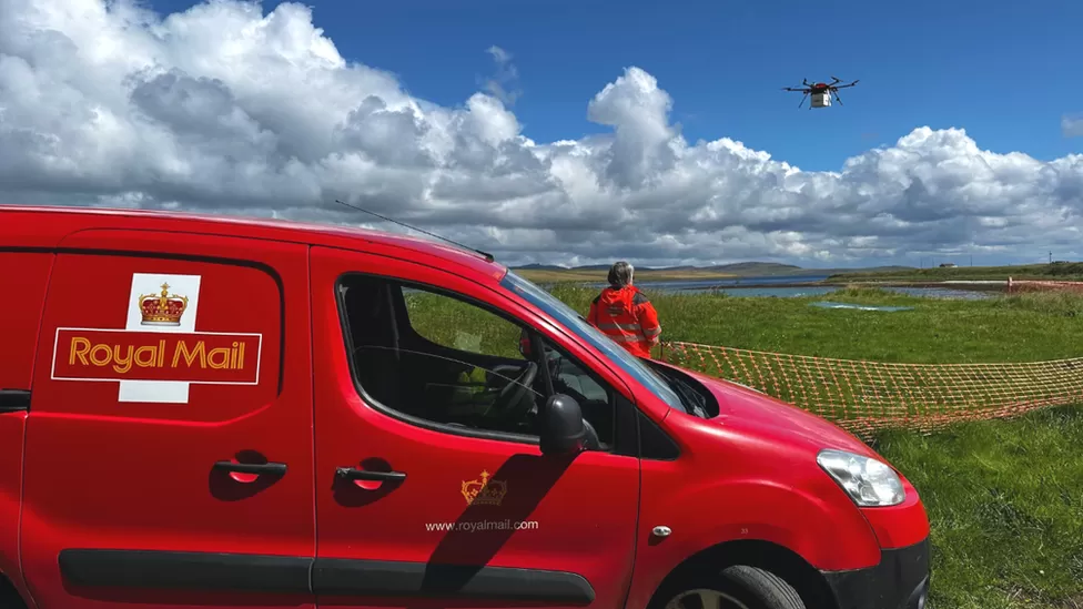 Postal worker beside royal mail van looking at new mail drone in air