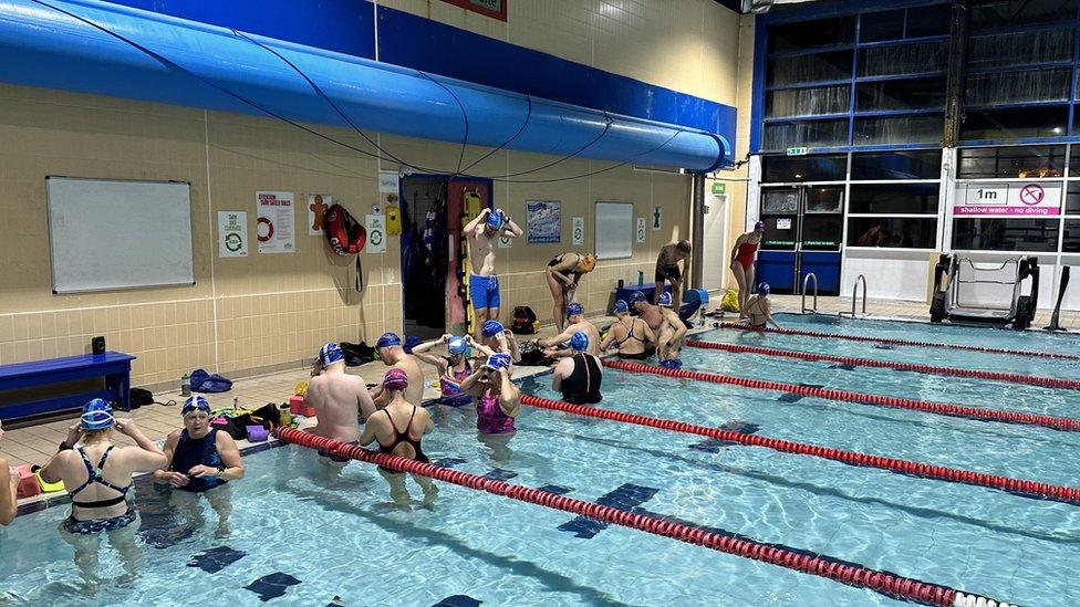 Swimmers in a laned pool wearing swimming hats while the windows show it is still dark outside