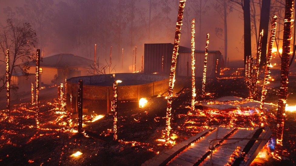 Remains of a structure burned by a bushfire continue to smoulder