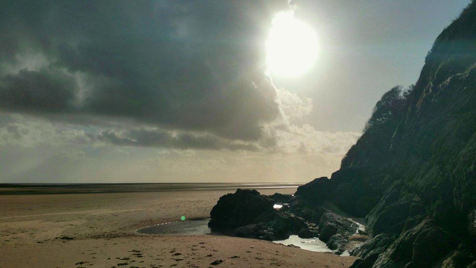 The sun peeping around the clouds on on Llansteffan beach on the Carmarthenshire coast