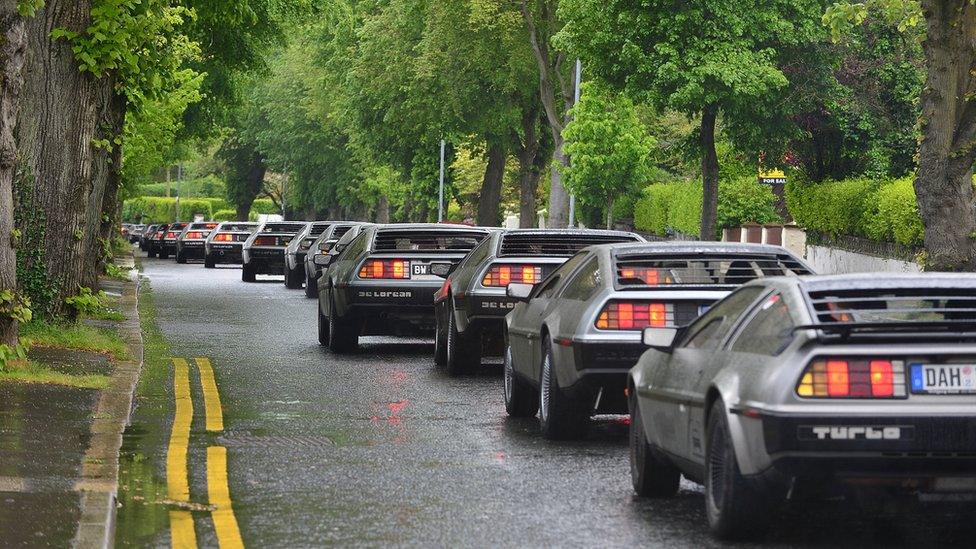 DeLorean cars drive along a tree-lined street