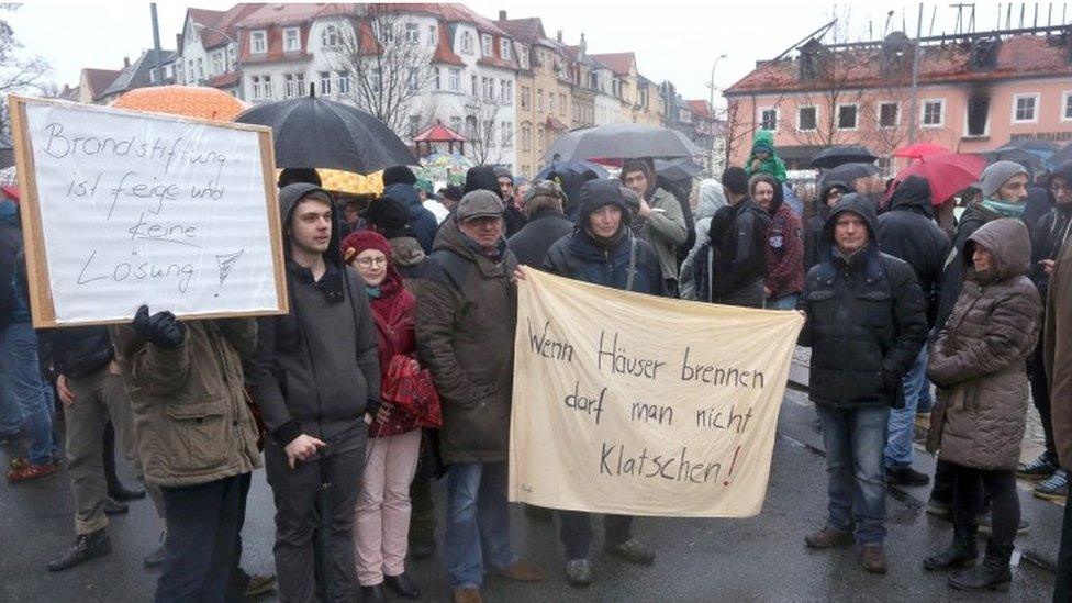 People hold up banners reading "Arson is cowardly and no solution" (left) and "When houses burn one cannot applaud" as they demonstrate in solidarity with refugees in front of a former hotel being converted into a home for asylum seekers and partly destroyed by a fire in Bautzen (21 February 2016)