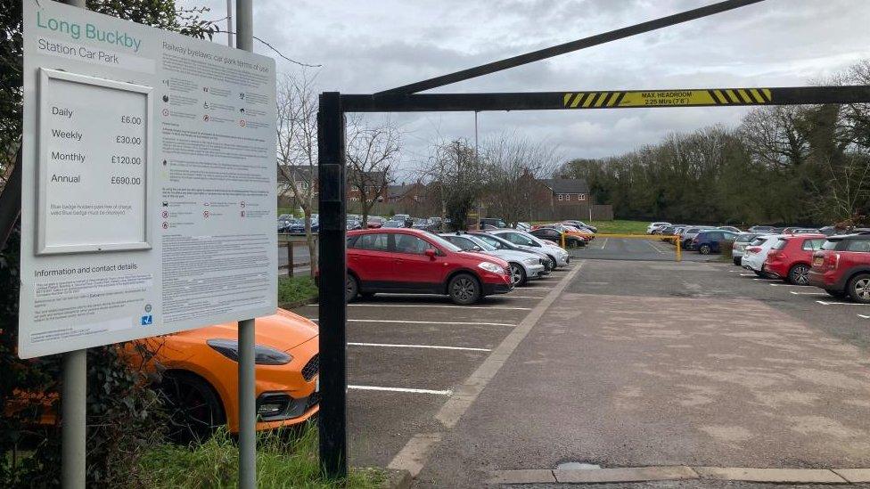 Car park showing sign in the foreground and cars in most of the spaces