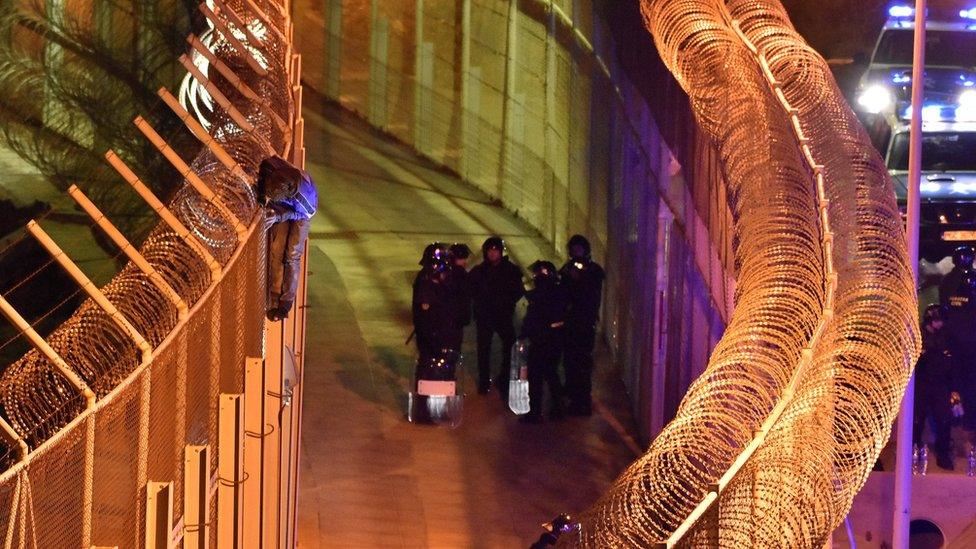 An African migrant stands on top of a border fence as Spanish police stand guard below during a failed attempt to cross into Spanish territories