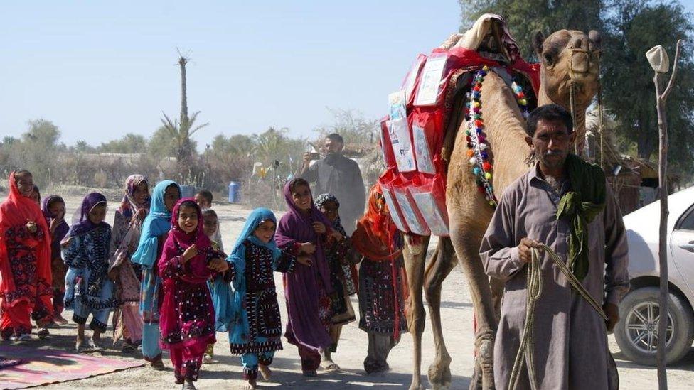 Children react as a camel carries books in Mand, Pakistan