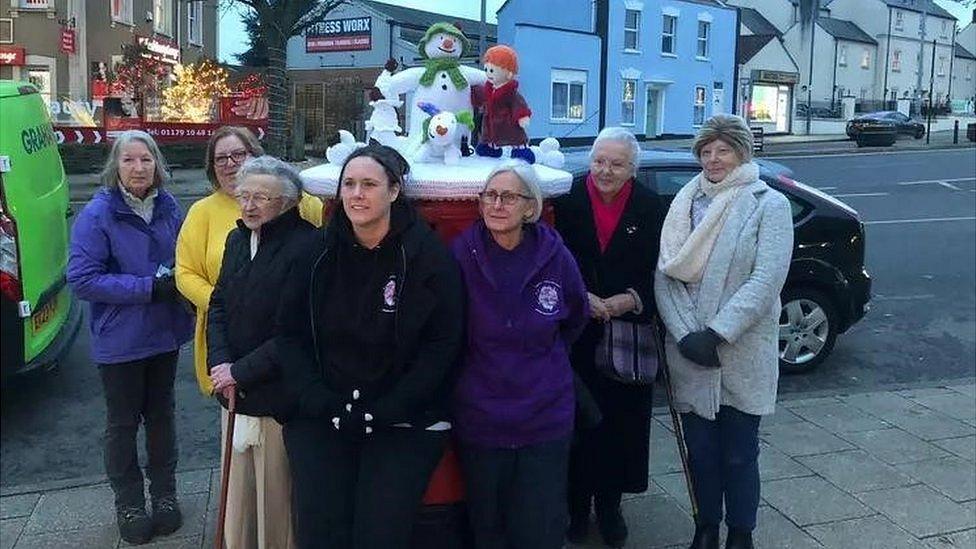 Women from the knitting group standing around their original Christmas post box topper