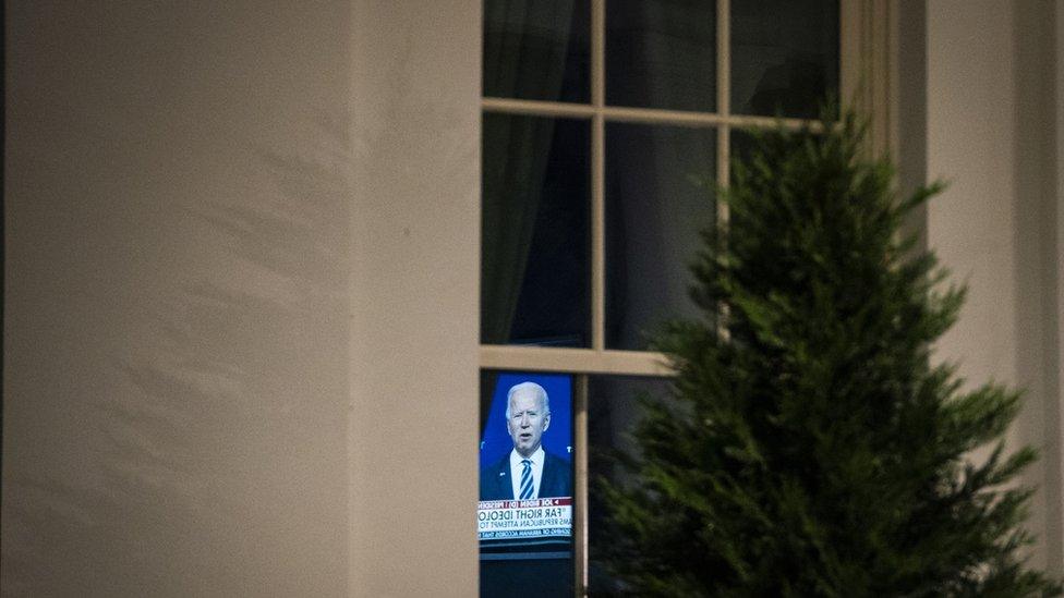 A television screen is seen through a window near the entrance to the West Wing at the White House.