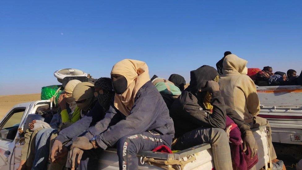 People sit in the back of trucks in the Sudanese desert