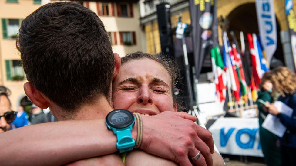 A runner hugs another competitor in relief having crossed the finish line