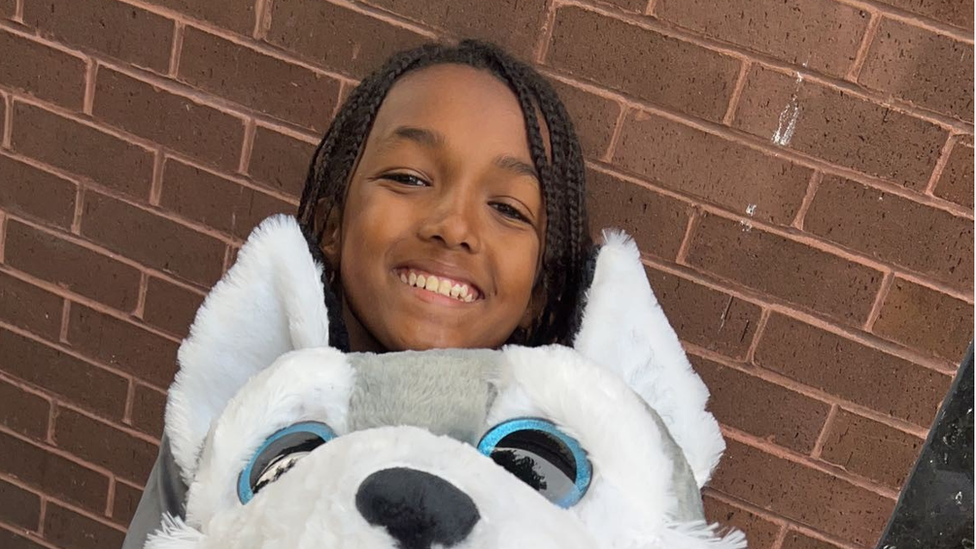 A young boy with plaited braids and a large teddy