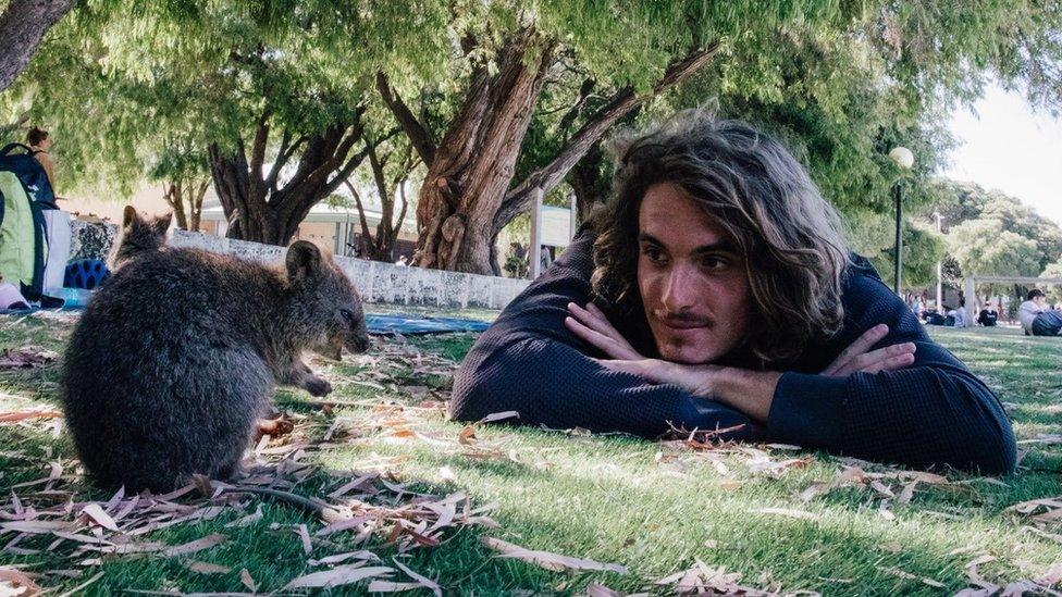 Stefanos Tsitsipas laying on the grass staring at an animal