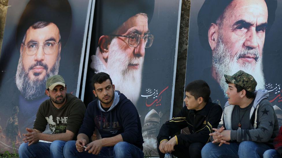 Lebanese sit in front of giant posters bearing portraits of Hassan Nasrallah, the head of Lebanon's militant Shiite Muslim movement Hezbollah (L), the founder of Iran's Islamic Republic, Ayatollah Ruhollah Khomeini (R) and Iran's supreme leader Ayatollah Ali Khamenei (C) during the funeral of a Hezbollah fighter