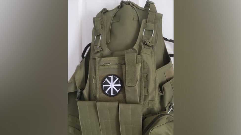 A khaki tactical vest with pockets on the side and front, with a black and white symbol at the front