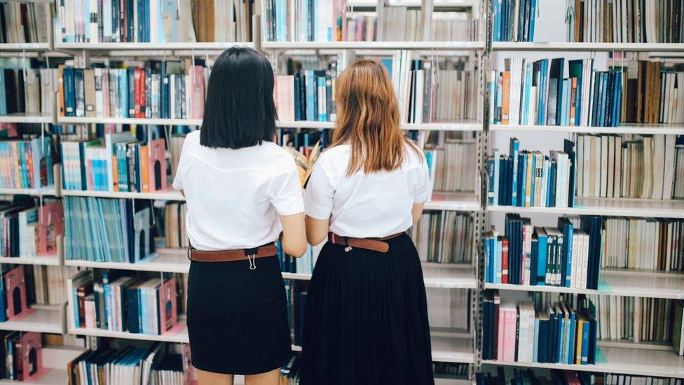 Two female students searching for books in a library - stock photo