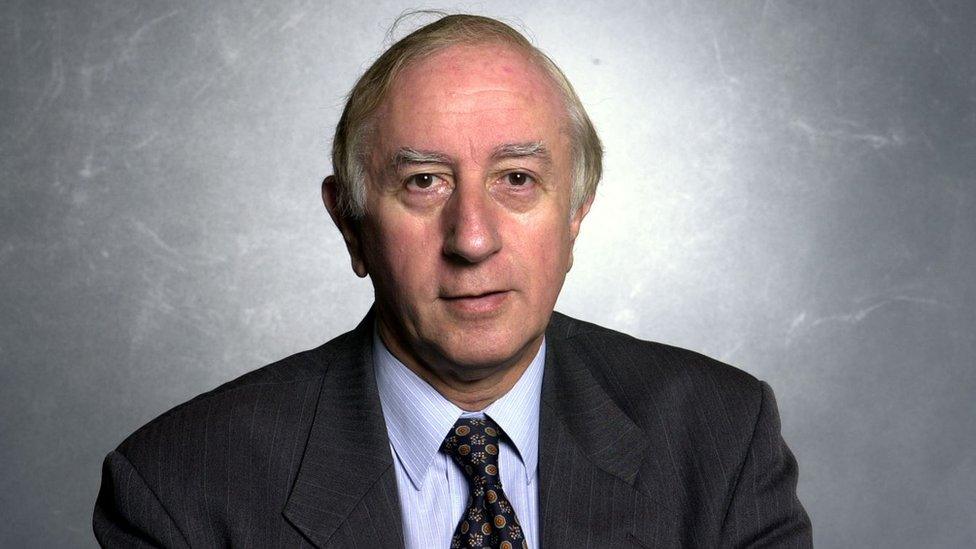 A man with white hair in a suit looking at the camera