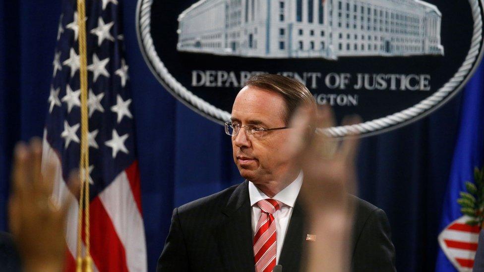 Rod Rosenstein is shown standing at a podium with the crest of the Justice Department hanging behind him.