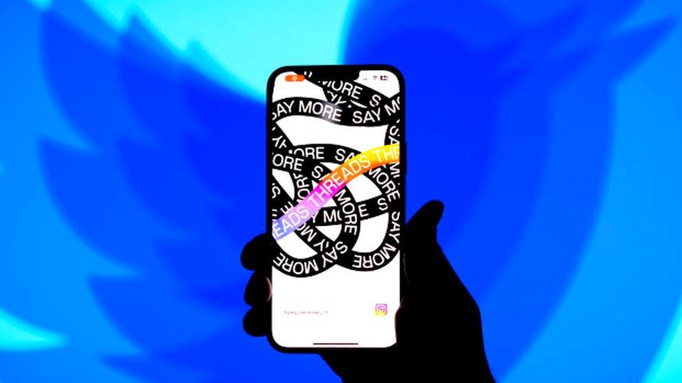 Threads app on a phone with a Twitter logo in the background.