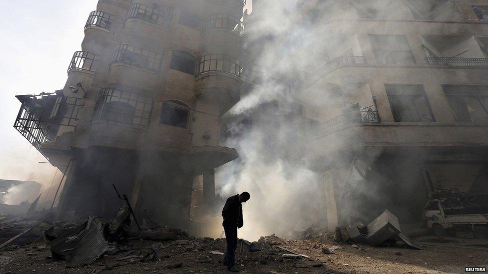 A man (with head bowed) walks in front of a burning building after a Syrian air force strike in Ain Tarma neighbourhood of Damascus January 27 2013