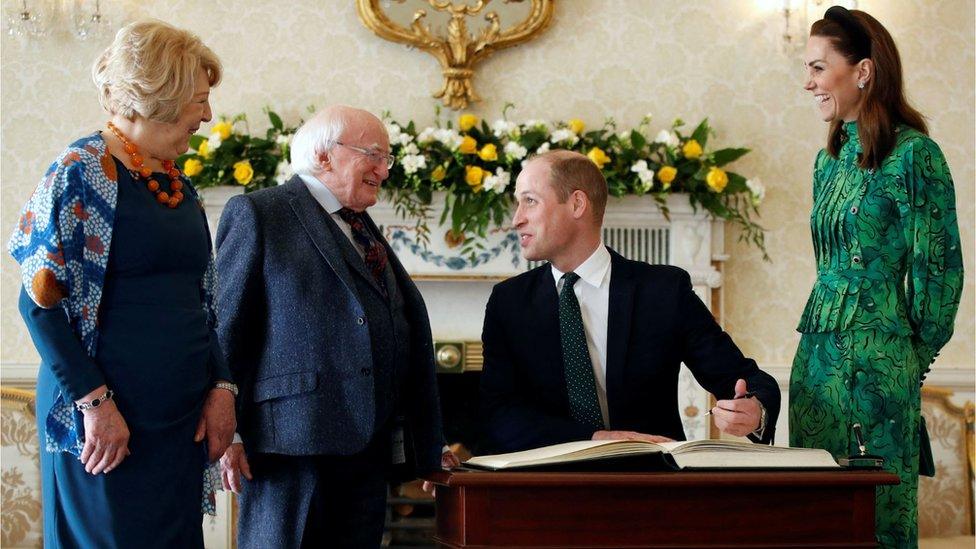 The Duke of Cambridge signs a visitors' book next to his wife Catherine as they meet Ireland's President Michael D Higgins and his wife Sabina