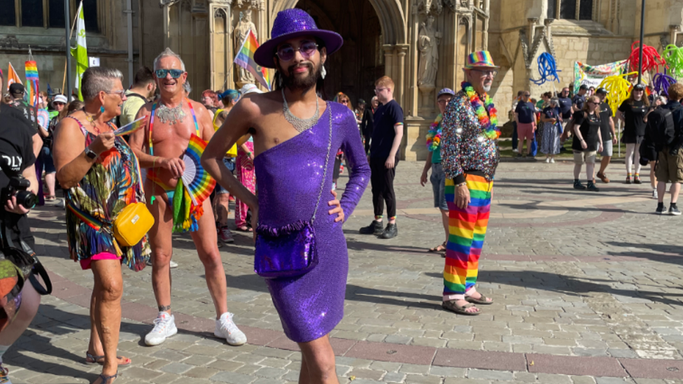 A person posing wearing a purple sparkly outfit