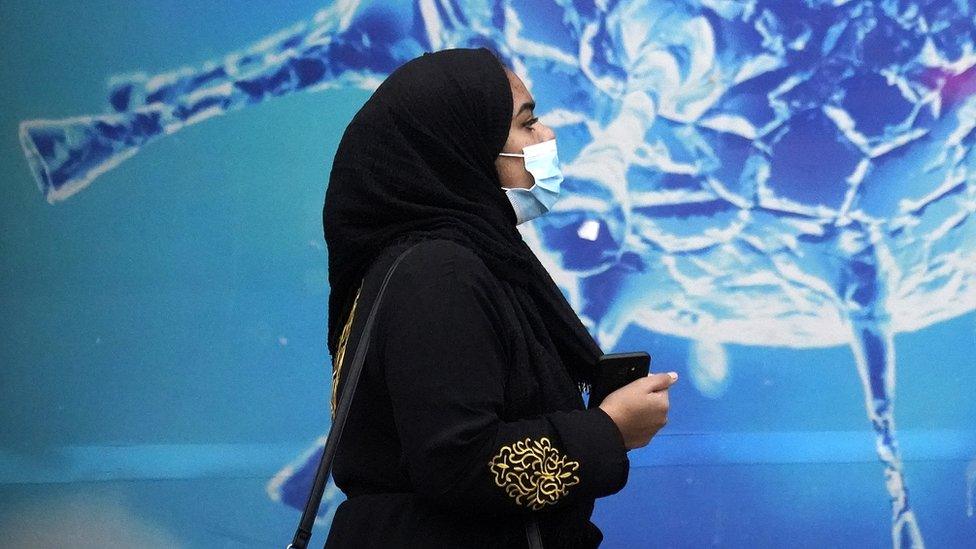 Woman wearing a face mask walking past an illustration of the coronavirus.