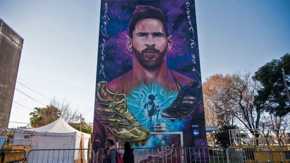 People walk past a giant mural depicting Argentinian football star Lionel Messi upon its unveiling in Rosario, Santa Fe, Argentina. - The mural, located in front of the school which Messi attended as a child, is the work of Argentinian artists Fer Lerena, Massi Ledesma, Lisandro Urteaga and Marlen Zuriaga