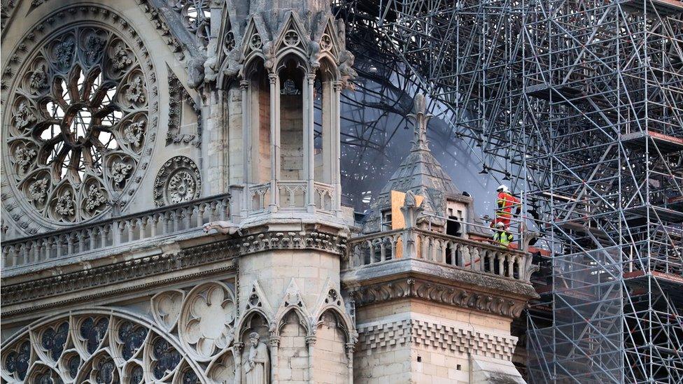 Firefighters stand on a balcony and observe damage from the fire