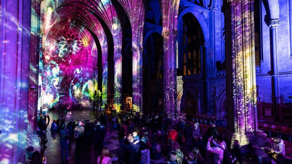 A crowd of people watch patterns of light on the walls of the cathedral