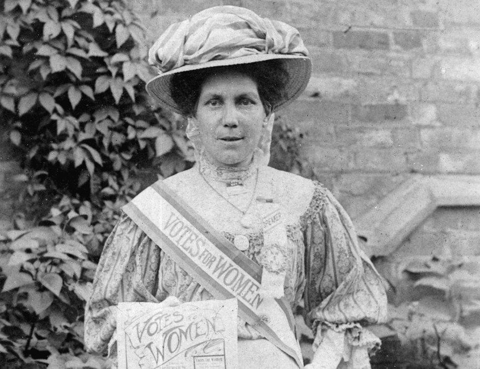 Alice Hawkins with a Votes for Women sash and poster