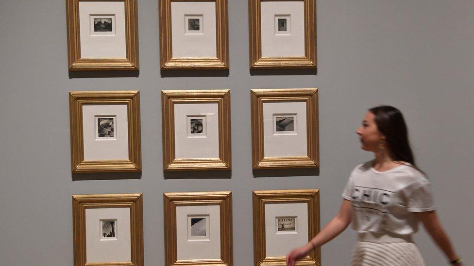 Woman stands in front of a group of photographs at the exhibition