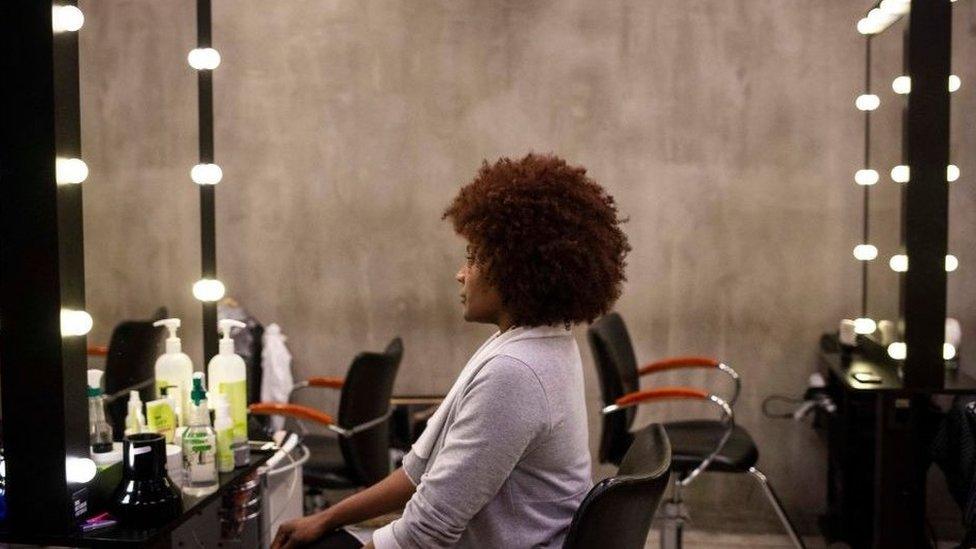 Woman sits in the mirror looking at her curly afro hairstyle