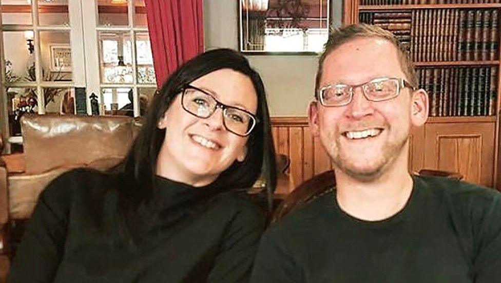 Kay Backhouse and her brother Syd Wilson sitting on a sofa smiling