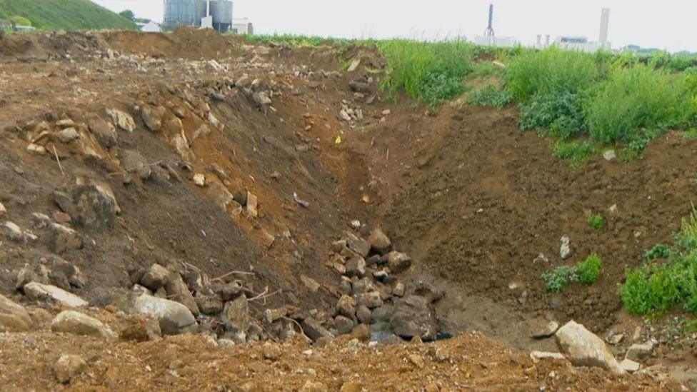 Some rubble in a hole surrounded by some grass on the right and dirt on the left. 