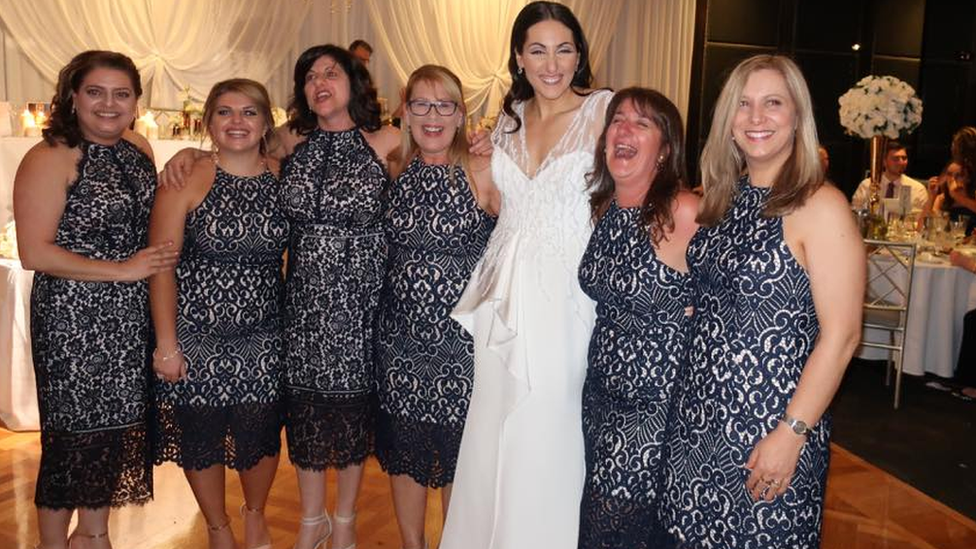 Six wedding guests in identical dresses pose for a photograph with the bride