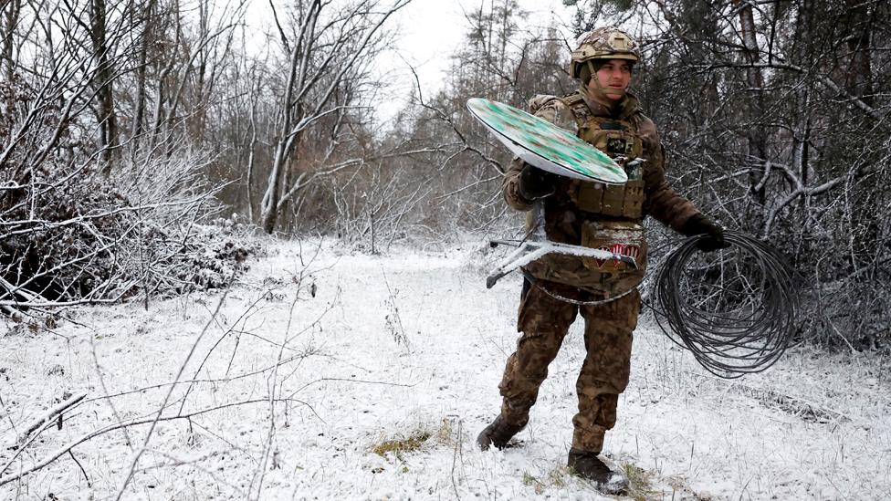 A Ukrainian serviceman walks with a disconnected Starlink terminal