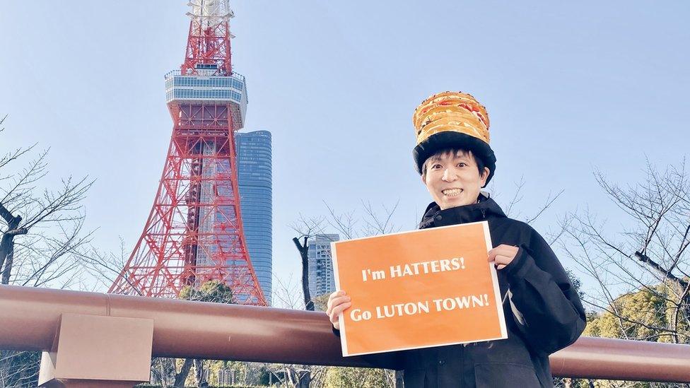 Sweets Nanako holding a sign that says "I'm Hatters, Go Luton Town" outside Tokyo tower