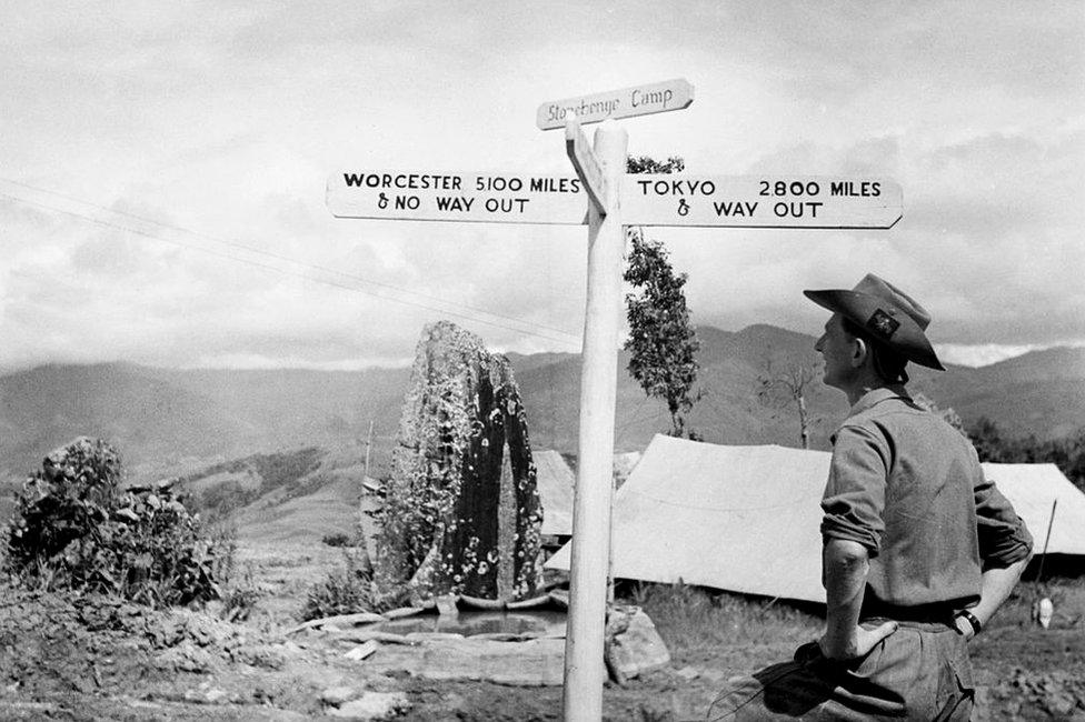 The British Army In Burma 1944 - a member of the Worcestershire Yeomanry views an amusing road sign beside an ancient standing stone at 'Stonehenge Camp' on the Imphal to Kohima road.