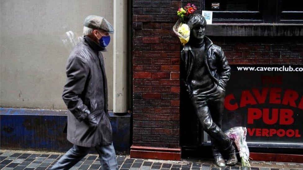 A man walks past John Lennon statue in Liverpool